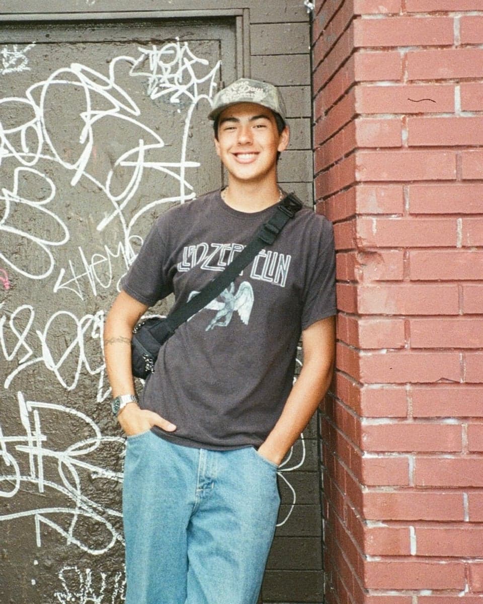 Carlos Flores smiling and leaning against a brick wall beside a graffiti-covered door