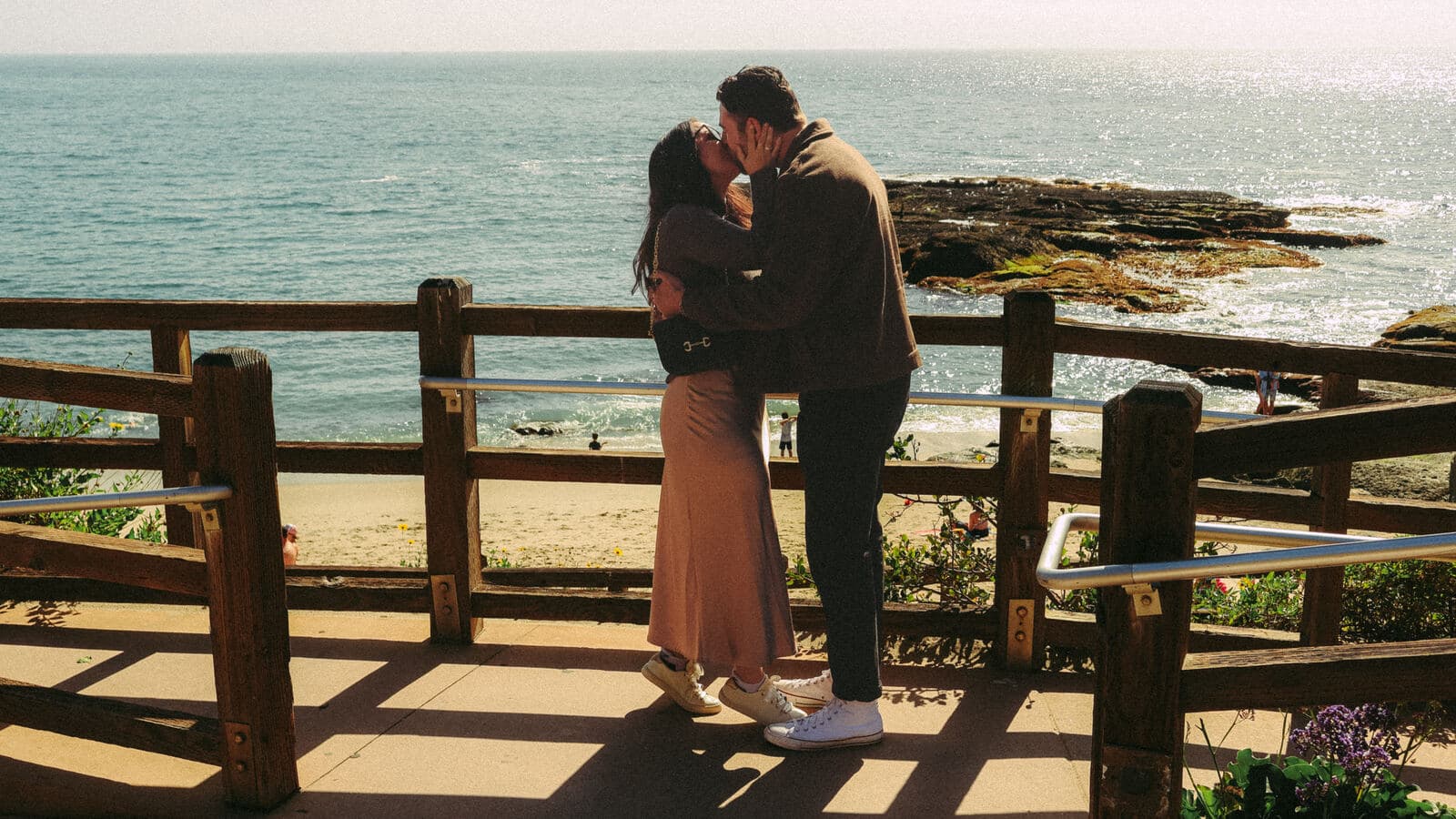 couple embracing and kissing at a wooden overlook above a sunny beach cove