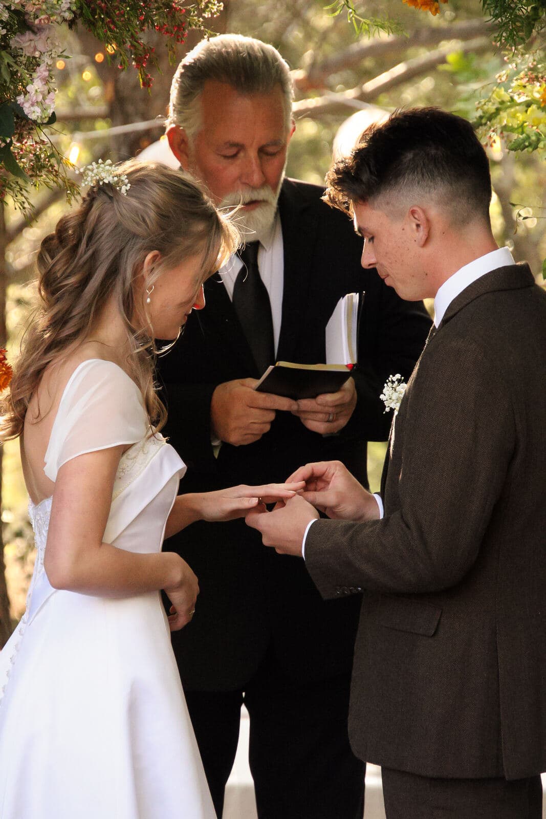 groom placing the ring on the bride's finger during an outdoor ceremony