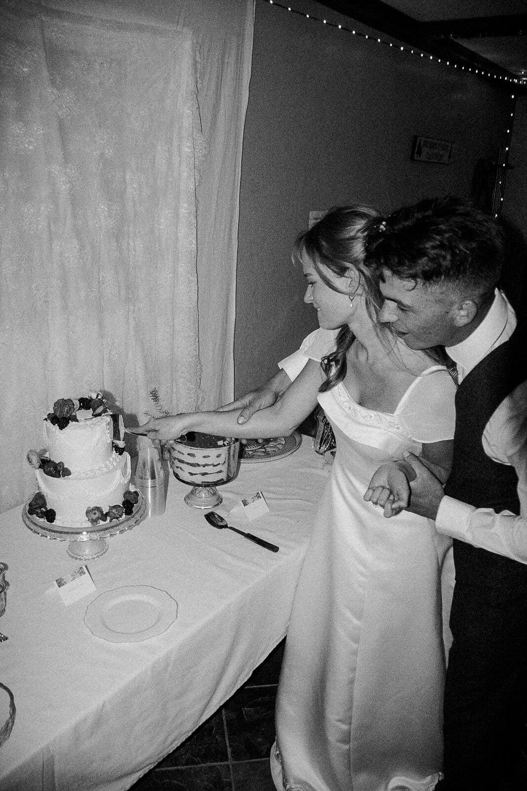 black and white photo of bride and groom cutting their berry-topped wedding cake