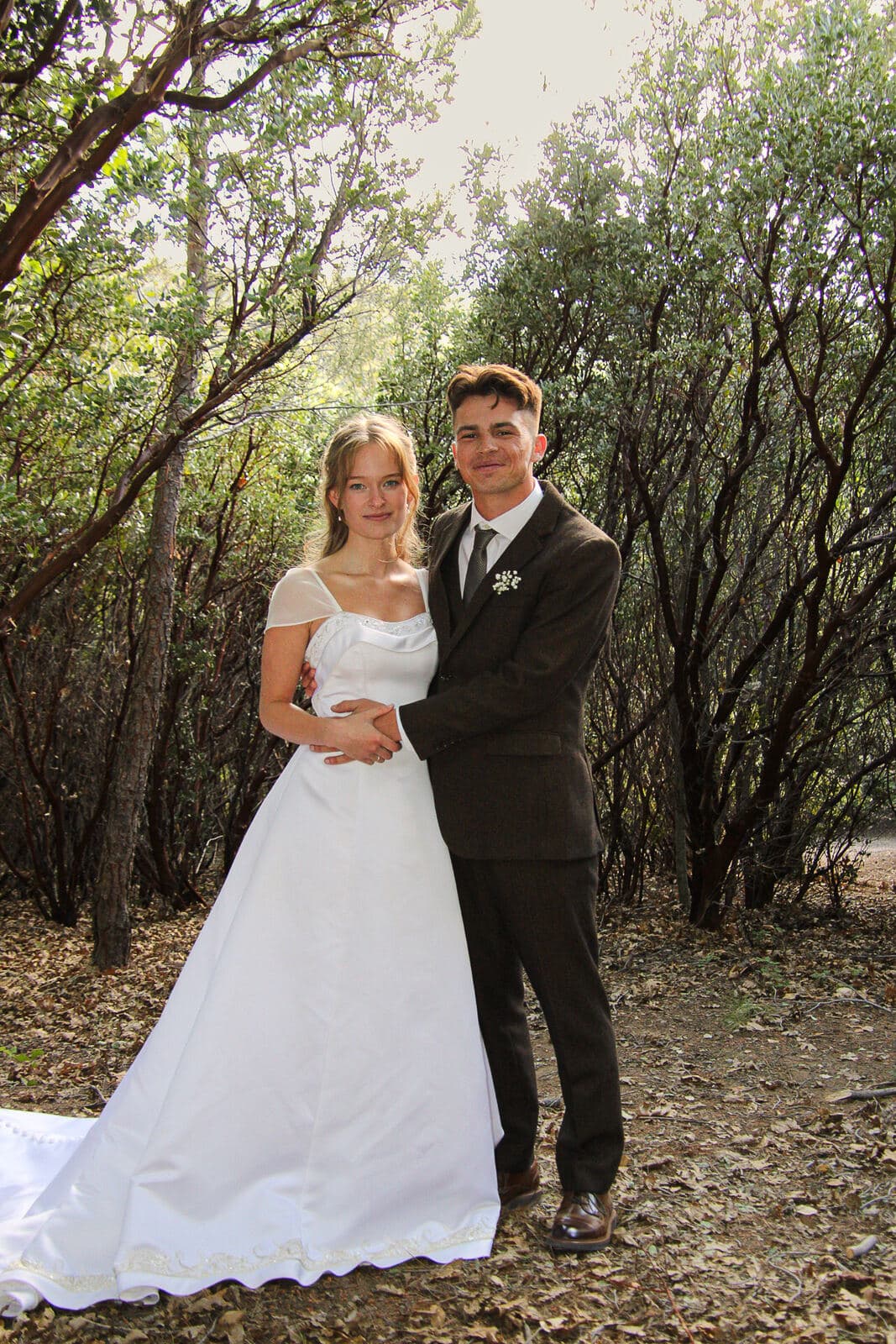 bride and groom posing hand in hand on a tree-lined trail with her train sweeping forward