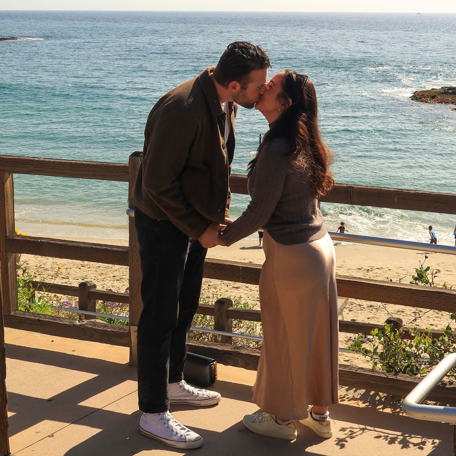 couple holding hands and kissing at a beachfront overlook on a sunny day