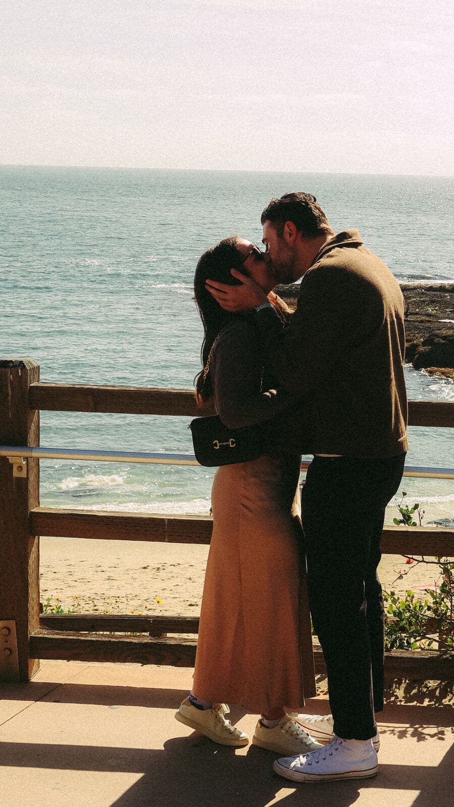 couple kissing tenderly at an oceanfront railing with waves in the background